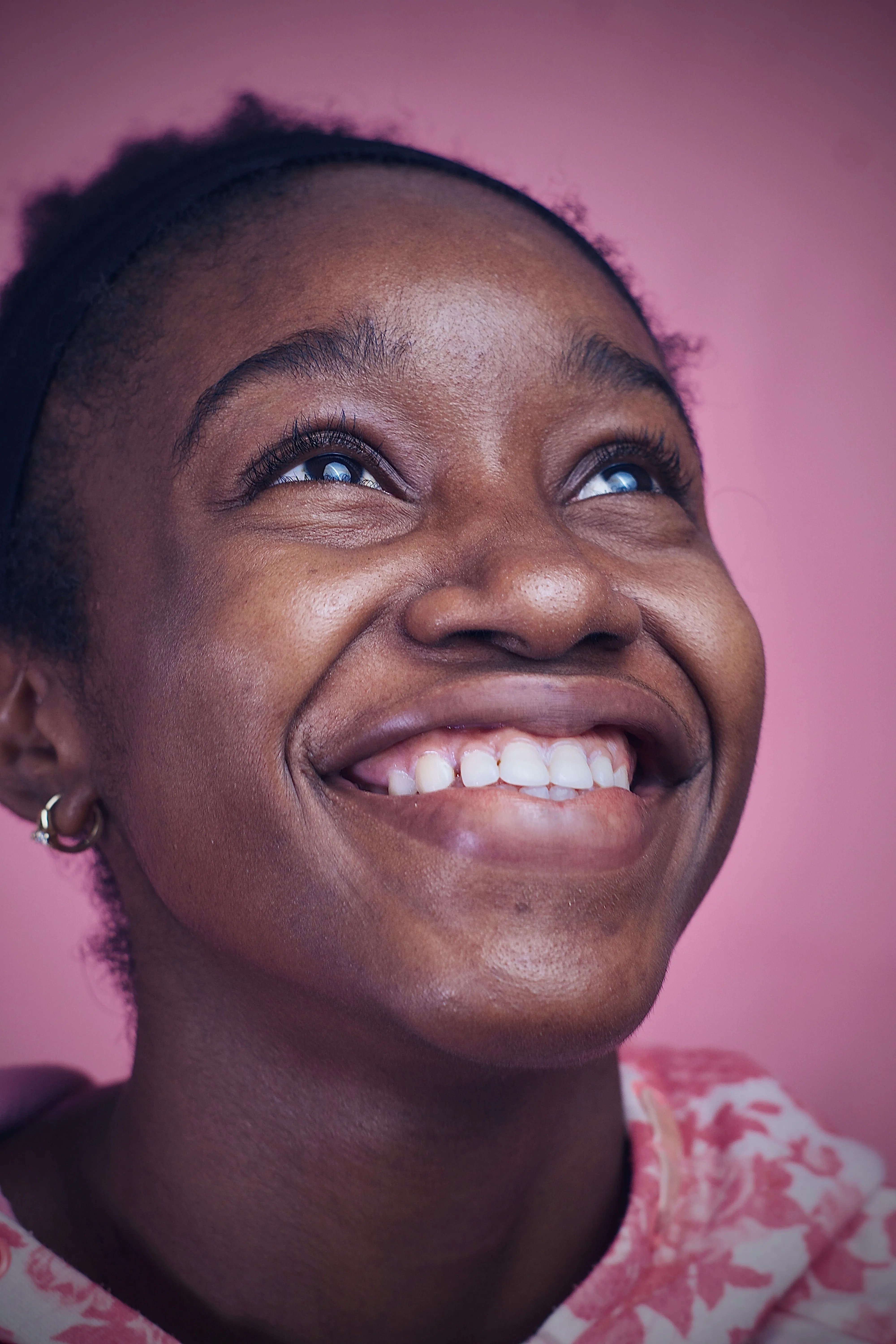 Young woman laughing joyfully, looking up against a soft pink background
